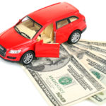 Red toy car with the front door open, sitting on four twenty-dollar bills that are fanned out on a white surface