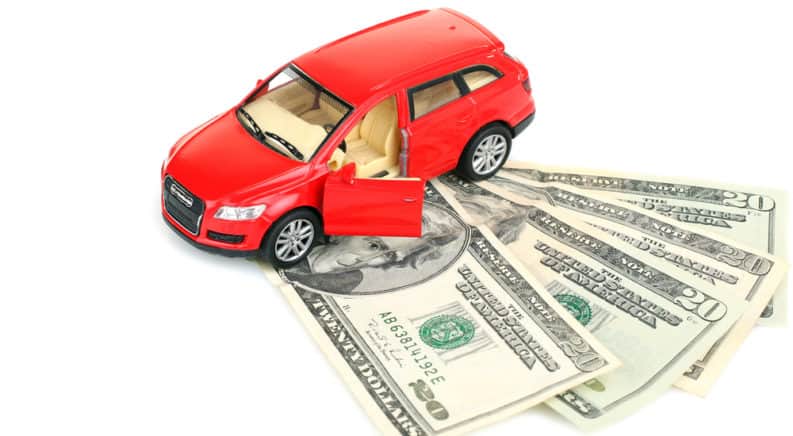Red toy car with the front door open, sitting on four twenty-dollar bills that are fanned out on a white surface