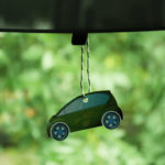Green car-shaped air freshener hanging from the rearview mirror of a vehicle
