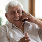 Old man sitting on a couch smiling with a phone to his ear