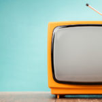 Orange tube TV with a grey screen sitting on a wooden floor in front of a blue wall