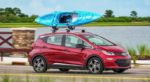 Red 2018 Chevy Bolt drives down past a lake with a blue kayak on the roof
