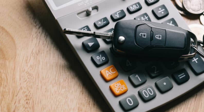Grey, black, and yellow calculator on a brown table with a black car key on top, next to silver change