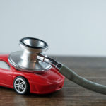 Silver and black stethoscope on top of a red toy car sitting on a brown table