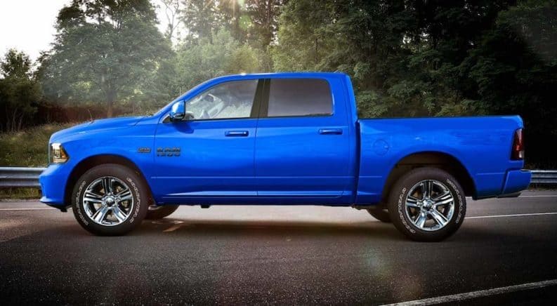 A backlit blue 2018 Ram 1500 Sport on a road in front of a woodline