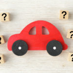 Red, wooden car sitting on its side, surrounded by wooden cubes with black question marks on them