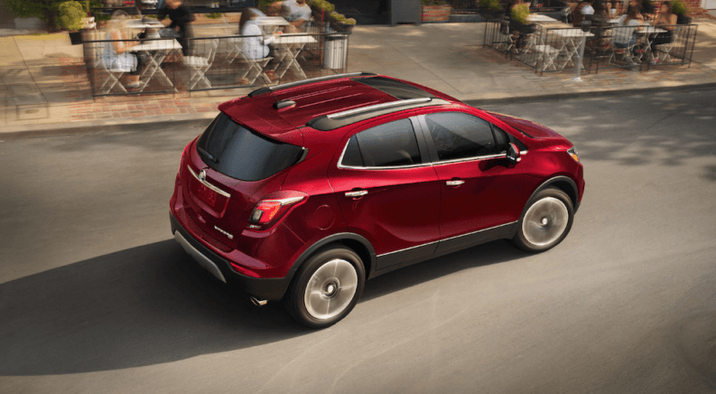 Red 2019 Buick Encore driving by cafe with tables and people