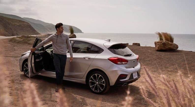 Man stepping out of silver 2019 Chevy Cruze hatchback at the beach