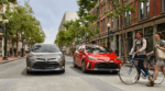 A gray and red 2019 Toyota Corolla on tree lined city street. Man and woman walking with bike