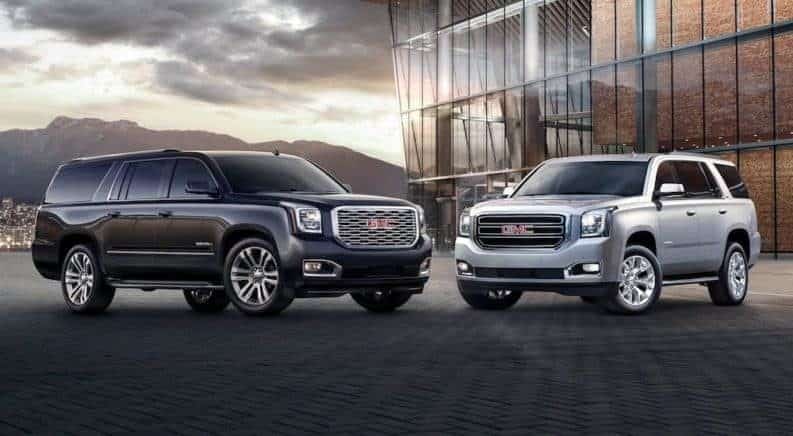 Black 2019 GMC Yukon XL and Silver Yukon in front of glass building