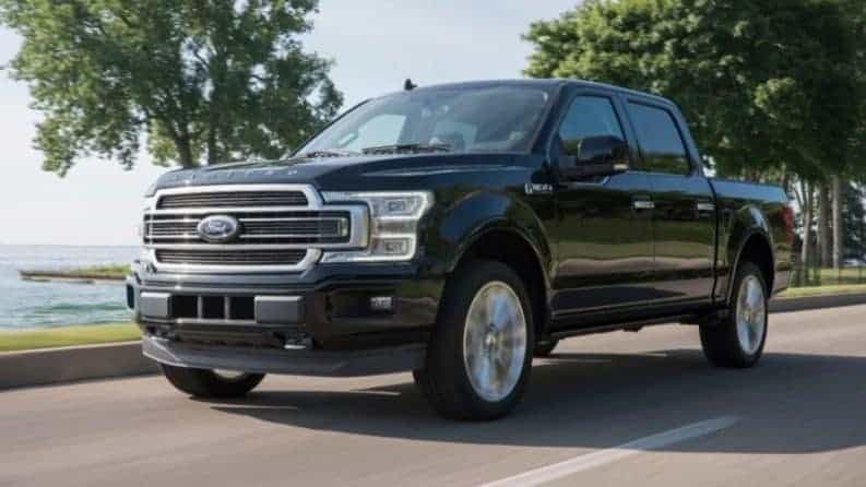 Black 2019 Ford F150 driving on road near water and trees