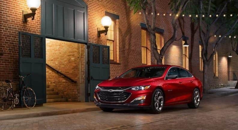 Red 2019 Chevrolet Malibu in front of red brick buiilding on tree-lined cobblestone road