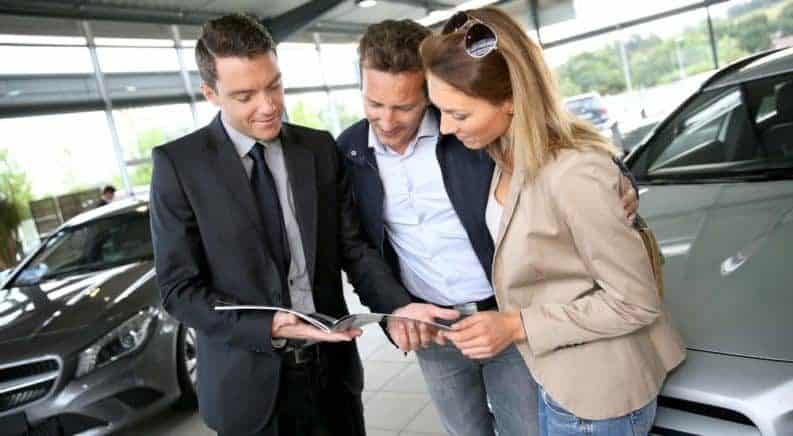 Couple in car dealership looking at brochure with salesman