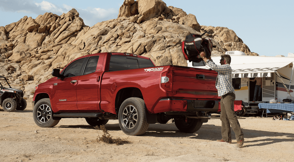 Man loading bag into red 2019 Toyota Tundra while camping with rocks in back