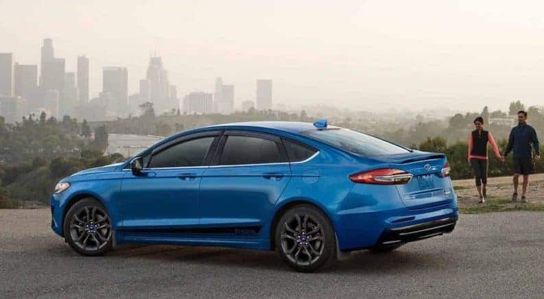 A bright blue 2019 Ford Fusion parked in front of a hazy city skyline