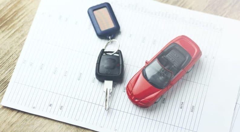 A red toy car and car keys on used car value research paperwork