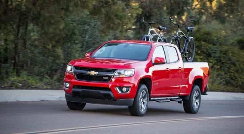 A red 2019 Chevy Colorado driving along a wooded road with bikes in the bed