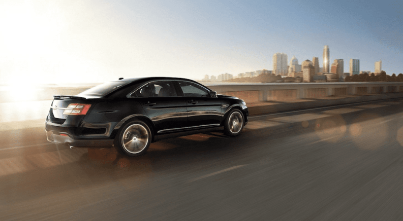 A black 2019 Ford Taurus on a highway with a city scape in back