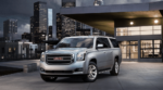 A silver 2019 GMC Yukon XL parked in front of a modern city building at night