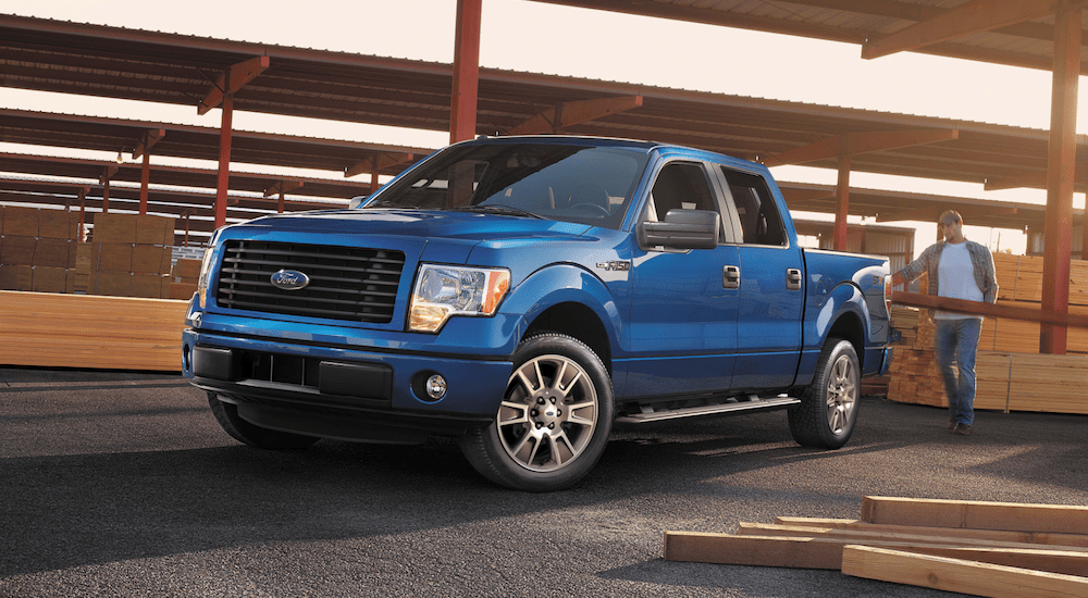 A man loads lumber into the back of a used blue 2014 Ford F150