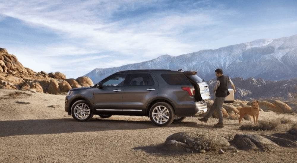 A man is opening the trunk to his 2016 used Ford Explorer in front of a mountain.