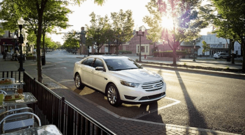 A white 2016 used Ford Taurus parked outside a cafe.