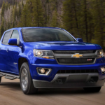 A blue 2019 Chevy Colorado is driving in front of pine trees. You can find Chevy trucks for sale at your Chevy Dealer.