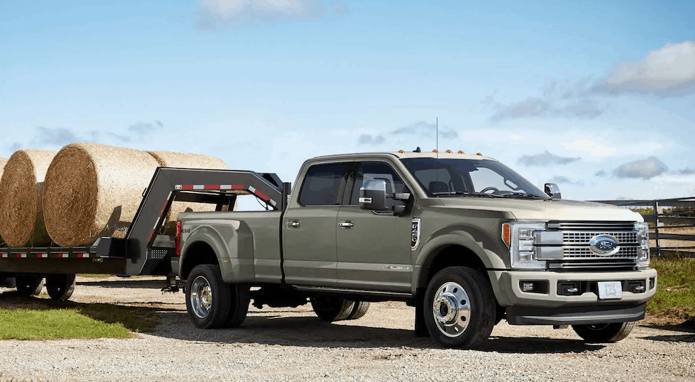 A silver 2019 Ford F-450 towing a gooseneck trailer with hay bales against blue skies
