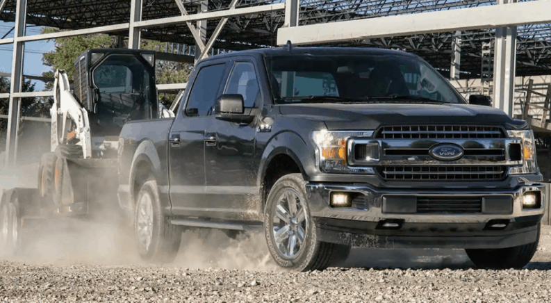 A black 2019 Ford F 150 towing a skid steer. It is one of the new diesel trucks for sale.