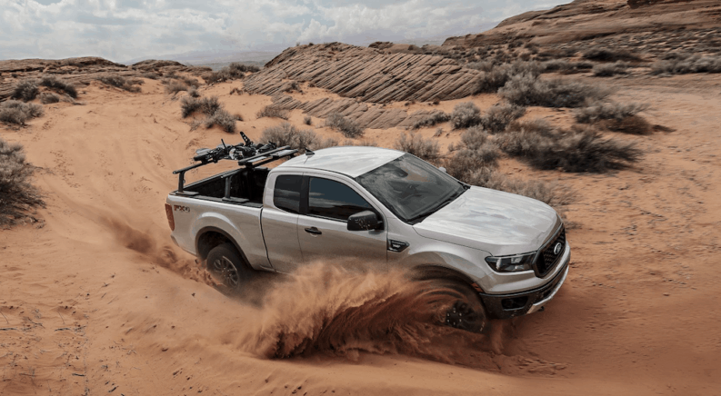 A silver 2019 Ford Ranger is taking a sharp corner in the desert with sand spraying. You can find Ford trucks for sale at a Ford Dealer.