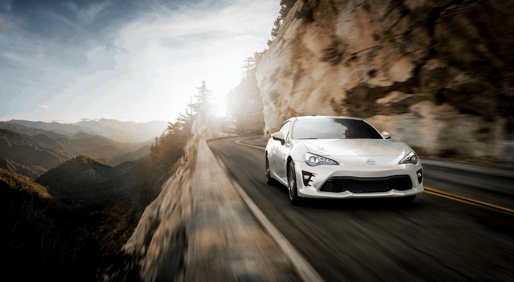 A white 2019 Toyota 86 sports car is driving a road along a cliff edge.