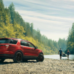 A red 2020 Ford Explorer next to a river with 2 people carrying a kayak