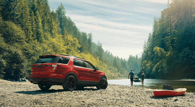 A red 2020 Ford Explorer next to a river with 2 people carrying a kayak