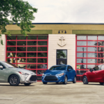 A silver, a blue, and a red 2019 Toyota Yaris sparked outside a garage in a city.