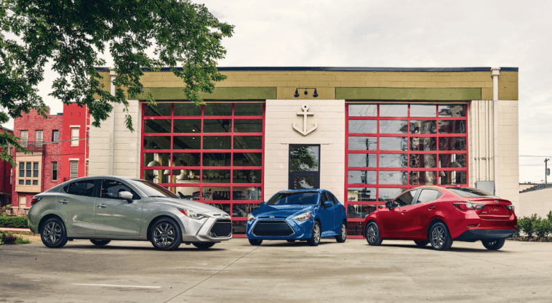 A silver, a blue, and a red 2019 Toyota Yaris sparked outside a garage in a city.