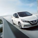A white 2019 Nissan Leaf is driving on a highway overpass.