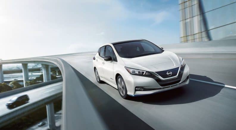 A white 2019 Nissan Leaf is driving on a highway overpass.
