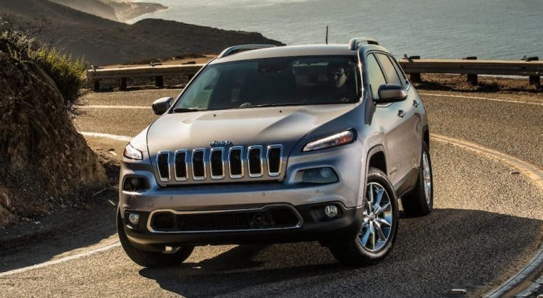 A grey 2017 Jeep Cherokee is driving around an inclining corner. Check out this model and other used Jeeps for sale at a local dealer.