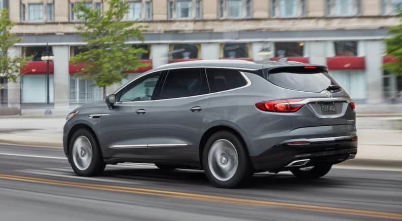 A grey 2019 Buick Enclave is driving past a city building.