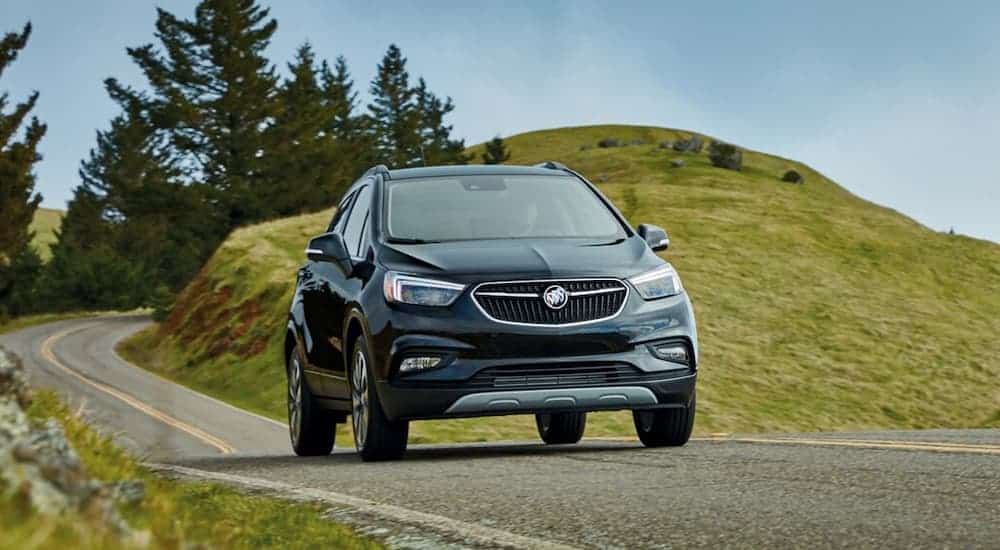 A black 2019 Buick Encore is driving in front of grassy hills. Check out performance when comparing the 2019 Buick Encore vs 2019 Hyundai Kona.