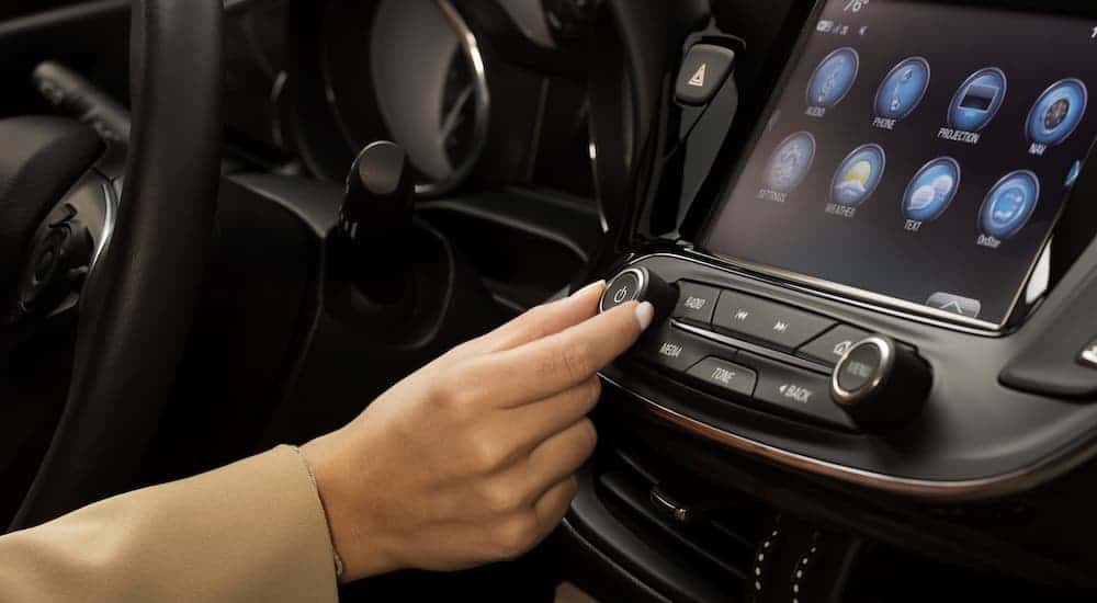 A woman's hand is turning the volume dial on the infotainment system in the 2019 Buick Envision, which wins when comparing the 2019 Buick Envision vs 2019 Ford Edge.