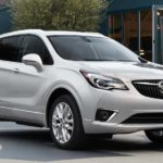 A siler 2019 Buick Envision is parked in front of shops.