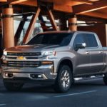A silver 2019 Chevy Silverado 1500 is parked in front of a wood and glass building.