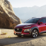 A red 2019 Hyundai Kona is parked next to a rock formation in the desert.