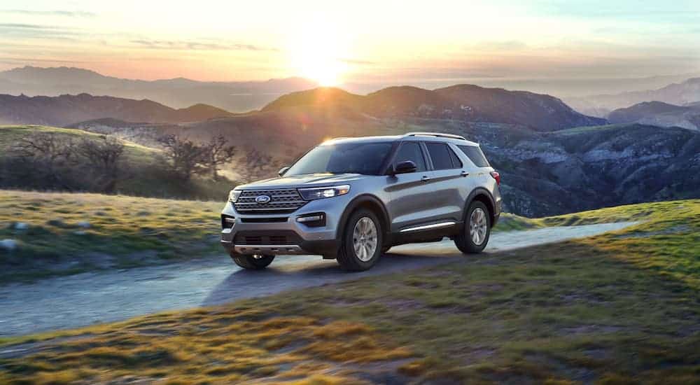 A grey 2020 Ford Explorer, available next year at a Ford dealership near me, is driving with a sunset and mountains in the distance.