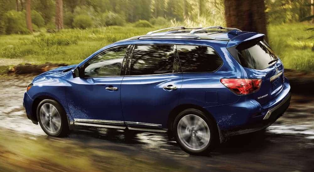 A blue 2019 Nissan Pathfinder is driving down a wet road in the woods.