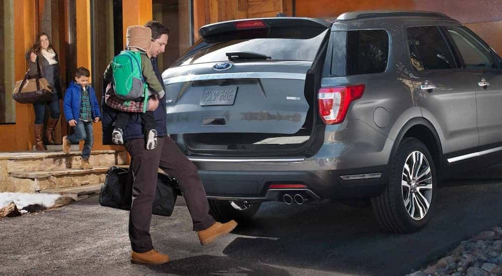 A man holding his child is using the liftgate feature on his grey 2019 Ford Explorer. Check out other features when comparing the 2019 Ford Explorer vs 2019 Chevy Traverse.