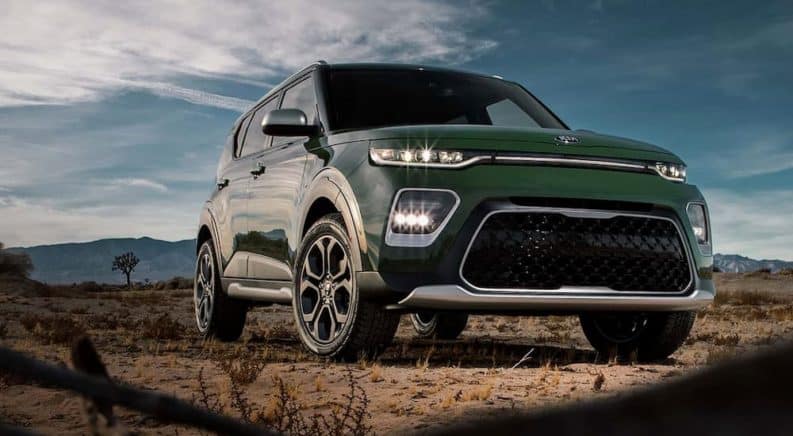 A green 2020 Kia Soul is parked in the dirt with mountains in the distance.