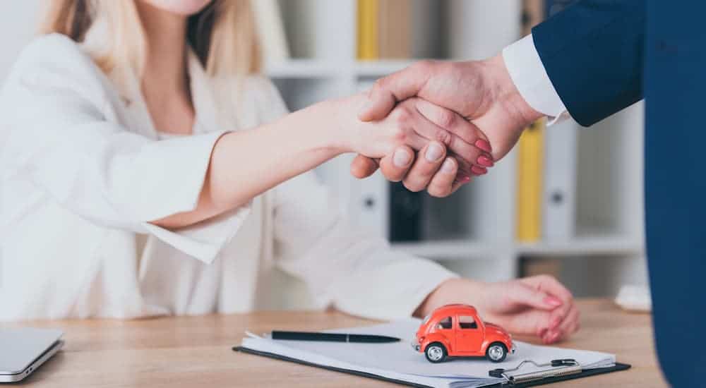 A closeup of a handshake over paperwork for a deal on used cars is shown.