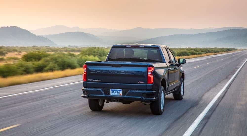 A blue 2019 Chevy Silverado 1500 is driving down a mountain highway with a sunset.